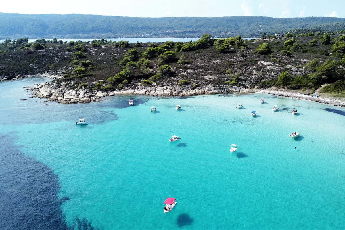 Vourvourou Beach view through pine trees, with clear blue water and untouched nature on Halkidiki.